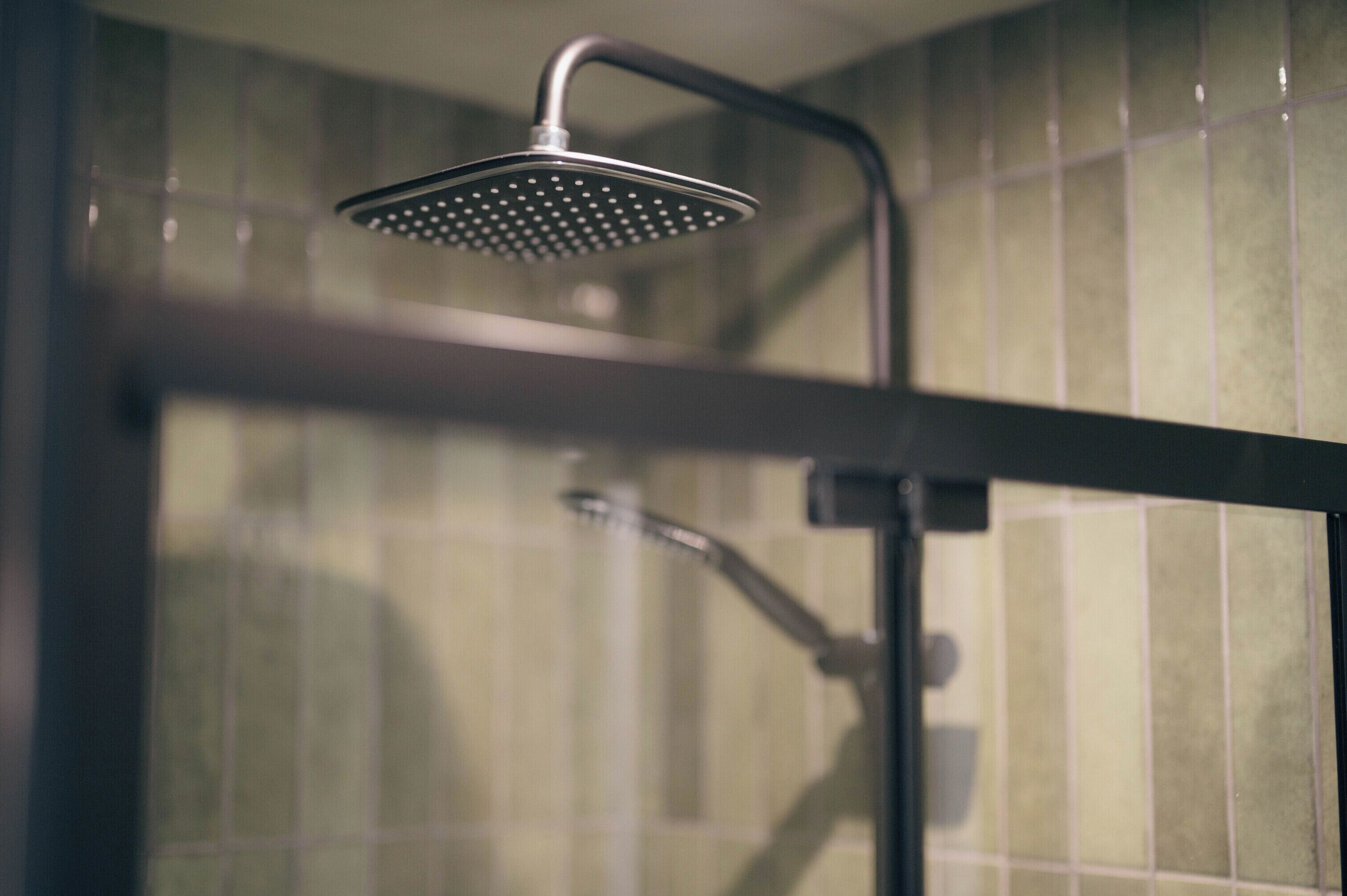A shower with a handheld head, a wall-mounted control panel, and a tiled wall.