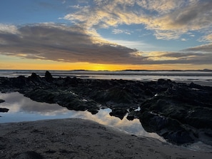 A rocky shoreline with calm water reflecting the sky. - Ffordd-Y-Wylan by Guestz (Rhosneigr)