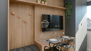A modern room with a built-in seating area, a flat-screen TV, a dining table with chairs, and a potted plant. - Sofisticação e Conforto no Coração do Moinhos (Porto Alegre)