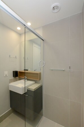 A modern bathroom with a glass shower enclosure, a white sink, and a wooden vanity. - Sofisticação e Conforto no Coração do Moinhos (Porto Alegre)