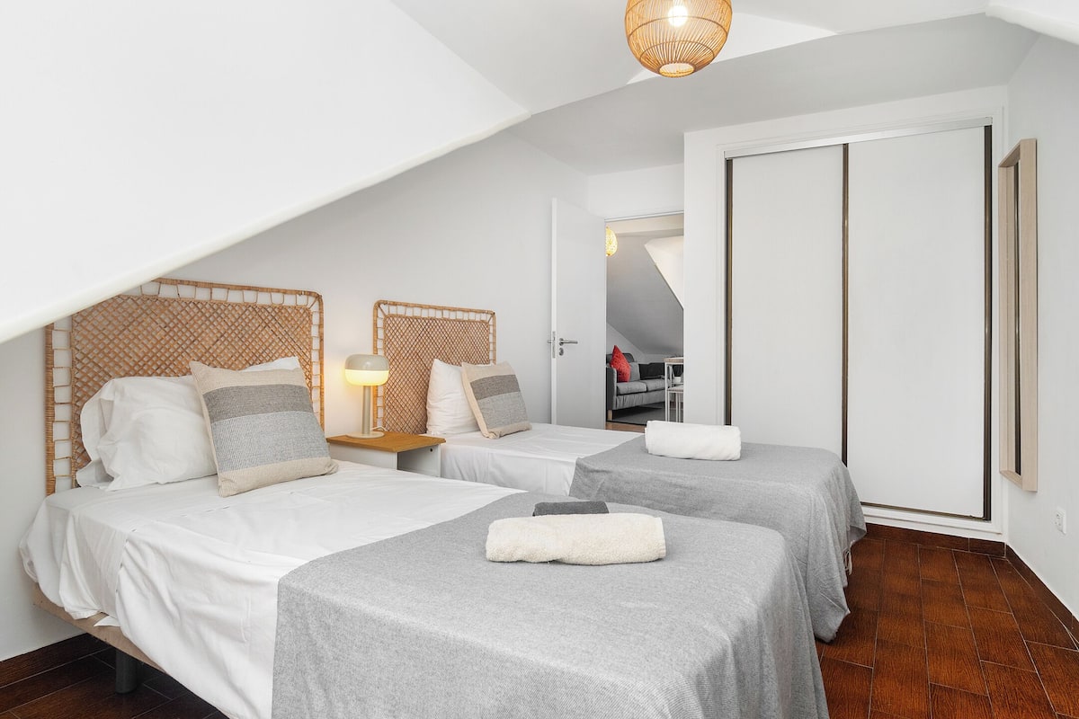 A room with two beds, a wooden headboard, a small table with a lamp, and a wardrobe.