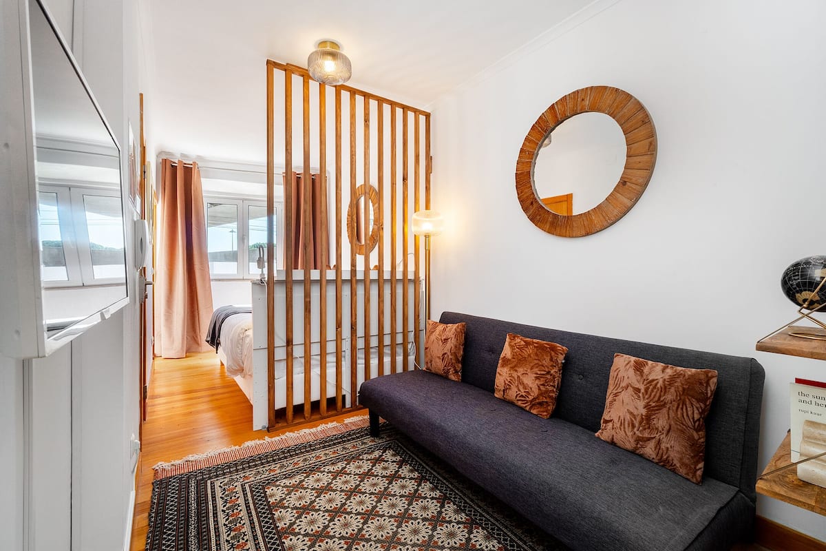 A modern living room with a sofa, patterned rug, wooden partition, and a round mirror on the wall.