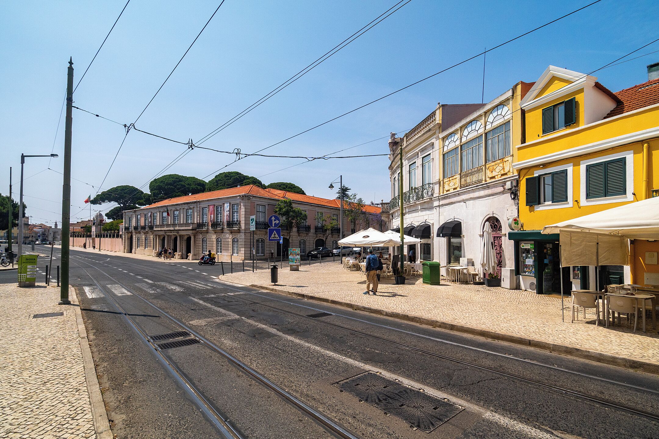 A street with tram tracks, buildings, and outdoor seating.