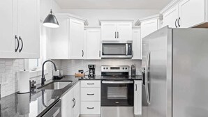 A modern kitchen with white cabinets, a stainless steel refrigerator, a microwave, and a stove.