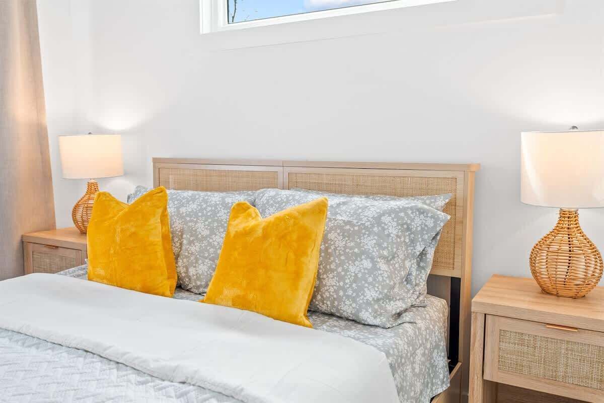 Een bed met een houten hoofdbord, twee nachtkastjes met lampen, en een raam boven het bed.