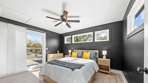A bedroom with a bed, a ceiling fan, a window, and a door.