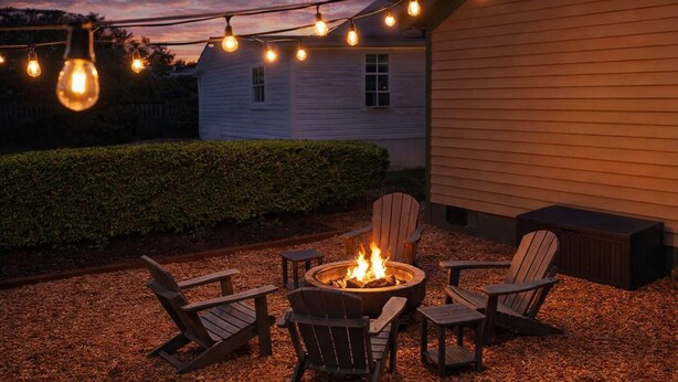 An outdoor seating area with a fire pit, wooden chairs, and string lights.