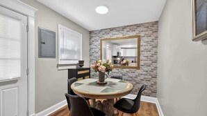 A dining area with a round table, four chairs, a vase with flowers, a brick wall, and a mirror.