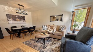 Una sala de estar moderna con comedor, un sofá, una mesa de centro y un ventanal grande.
