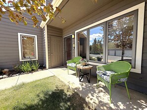 Un patio cubierto con dos sillas de mimbre verde, una mesita y una puerta que da a la casa.
