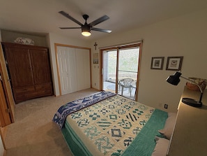 A bedroom with a bed, a ceiling fan, a door, and a window.