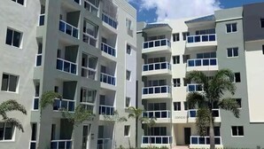 A multi-story building with balconies, a parking lot, and palm trees. - Modern Apartment Comfortable & Quiet (Santo Domingo Este)