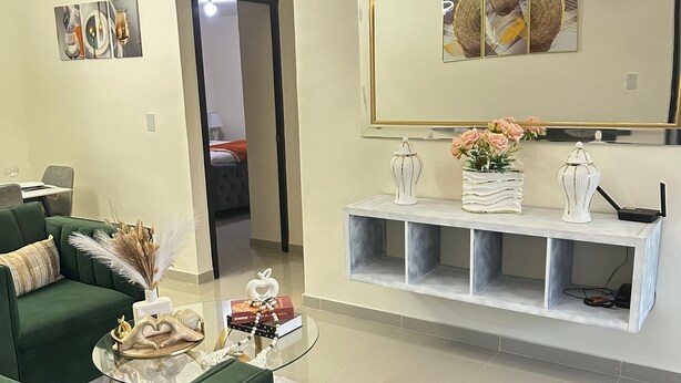 A modern living room with a green sofa, a glass coffee table, and a decorative mirror. - Modern Apartment Comfortable & Quiet (Santo Domingo Este)