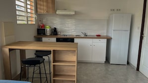 Een kleine keuken met een houten tafel, twee barstoelen, een magnetron, een koffiezetapparaat, een spoelbak en een witte koelkast.