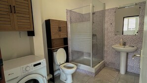 Een badkamer met een wasmachine, toilet, douche en wastafel.