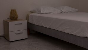 Een slaapkamer met een bed, twee kussens, een nachtkastje met een lamp en een ladekast.