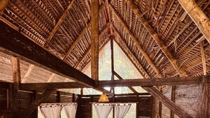 A wooden cabin with a thatched roof, two beds, a small table, and a fan. - nawala eco-hostel (Nuquí)