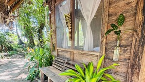 A rustic wooden building with a bench outside, surrounded by greenery. - nawala eco-hostel (Nuquí)