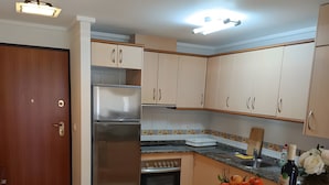 A kitchen with a refrigerator, oven, and a bowl of oranges on the counter. - Puerto Marina Apartment with Mountain Views, Wi-Fi, and Air Conditioning (Los Alcázares)