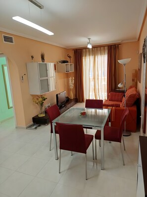 A dining area with a glass table, red chairs, a sofa, a TV, and a cabinet. - Apartment 'Puerto Marina Bajo' with Shared Pool, Wi-Fi and Air Conditioning (Los Alcázares)