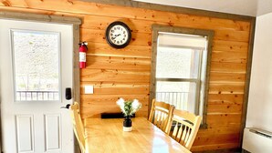 Una habitación con paneles de madera, una mesa de madera, cuatro sillas, un reloj de pared y un extintor.