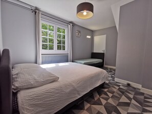Ein Schlafzimmer mit einem Bett, einem Fenster mit Vorhängen, einem Nachttisch, einem Spiegel und einem gemusterten Boden.