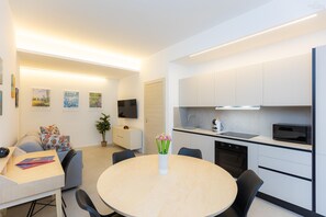 A modern kitchen with white cabinets, a microwave, and a sink. There's a dining area with a round table and chairs, and a TV mounted on the wall. - Sivori apartment in the Prati neighborhood (Rome)