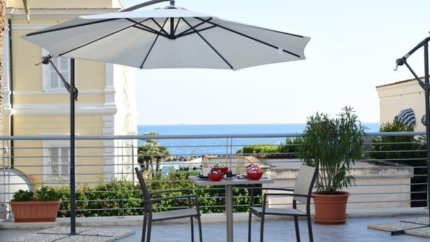 A terrace with a table and chairs, an umbrella, potted plants, and a view of the sea. - Aria di Mare (Santa Marinella)