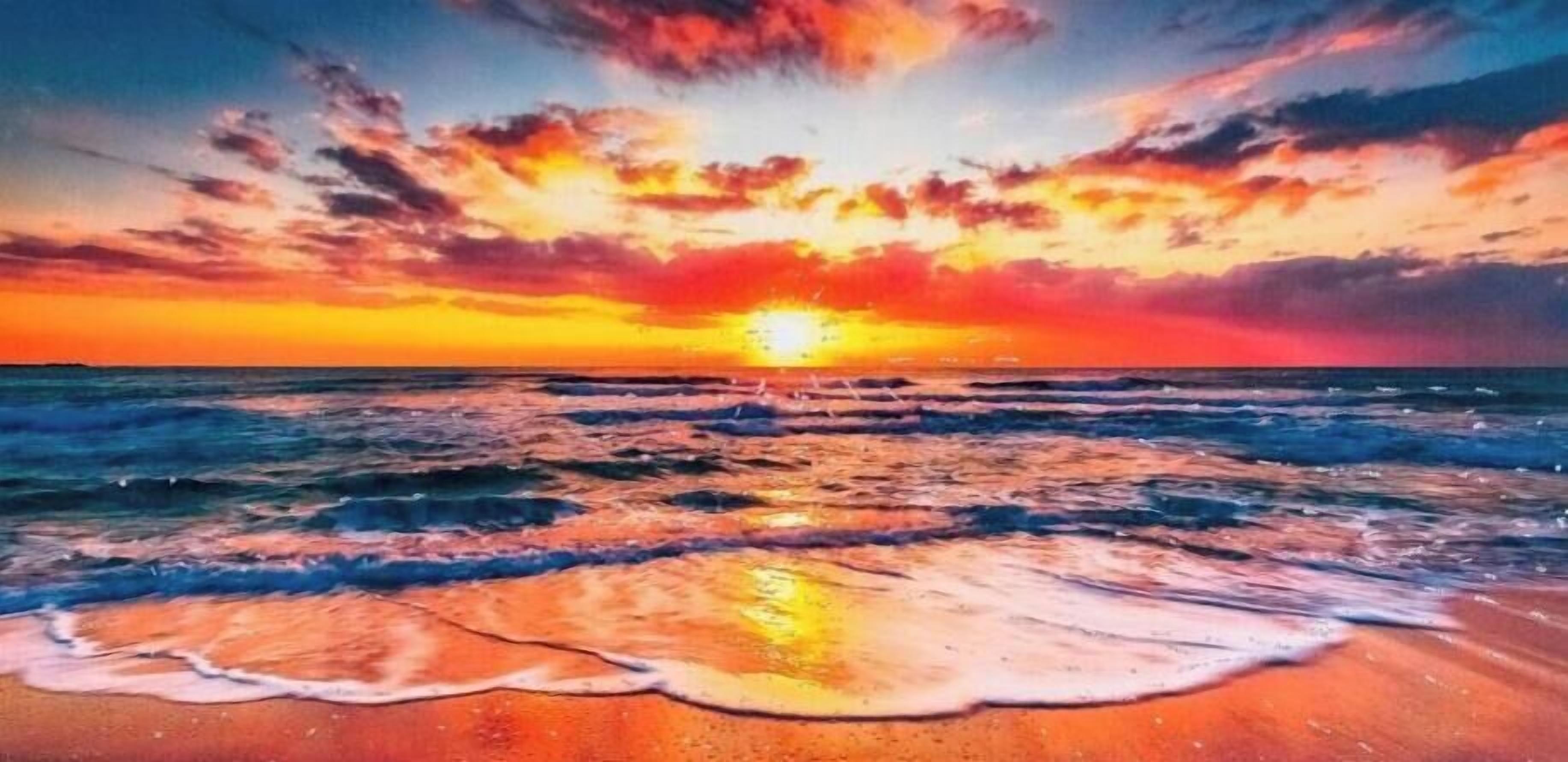 A sunset over the ocean with waves on the shore.
