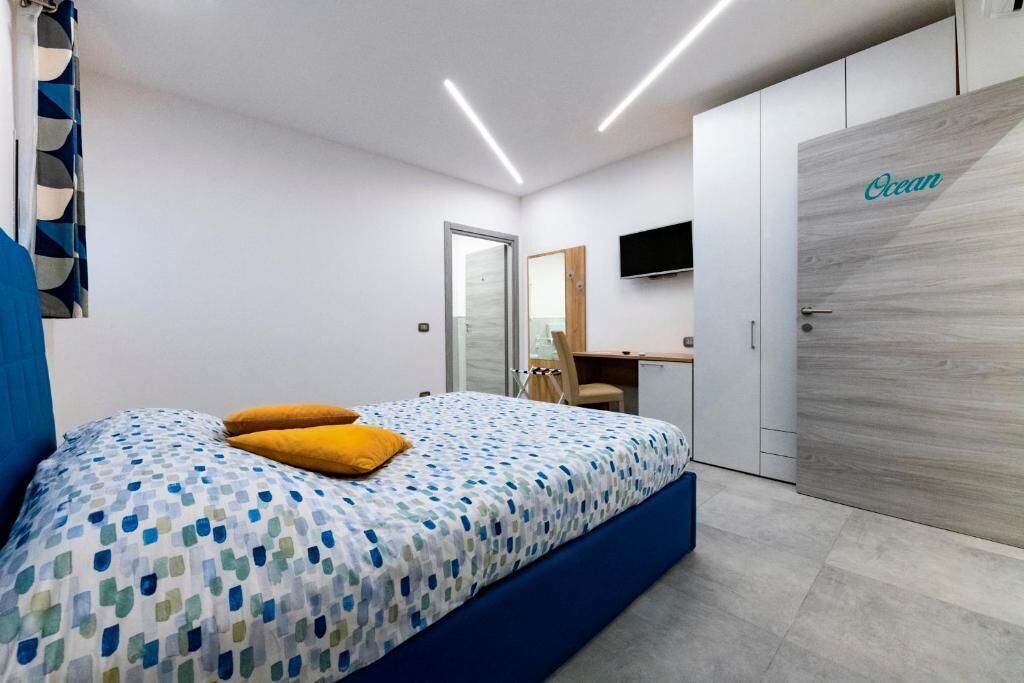 A bedroom with a bed, a desk, a chair, a wardrobe, and a television.