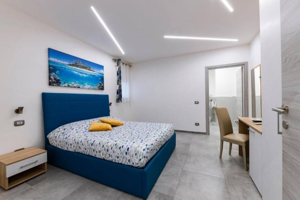 Ein Schlafzimmer mit Bett, Schreibtisch, Stuhl, Gemälde und einer Tür.