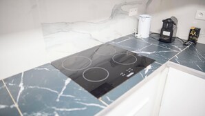 Une cuisine dotée d’un plan de travail en marbre noir, d’une plaque de cuisson intégrée avec quatre brûleurs, d’une machine à café et d’une boîte de capsules de café.
