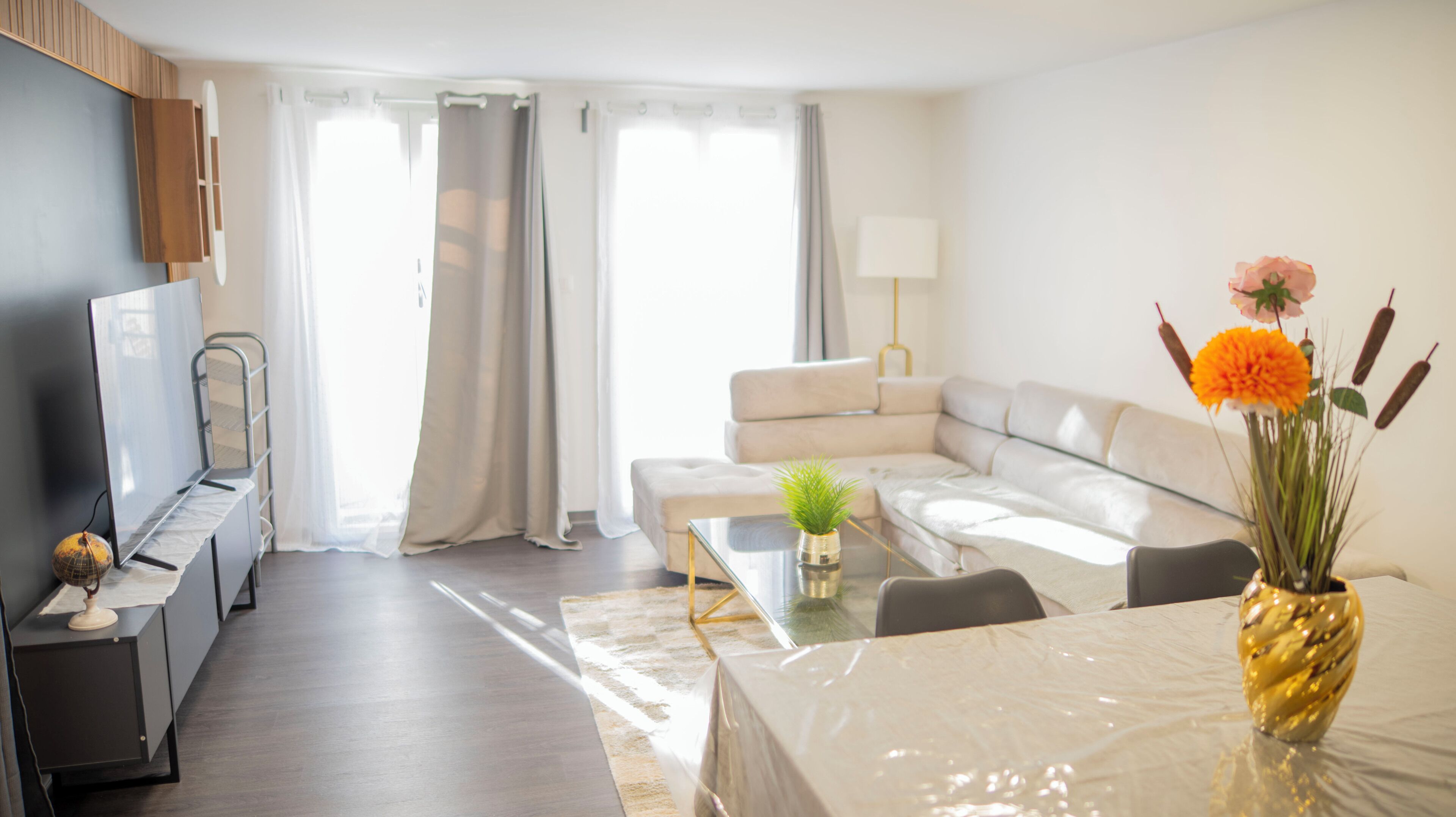 Ein modernes Wohnzimmer mit einer Couch, einem Glastisch, einem Fernseher und einer dekorativen Vase mit Blumen.