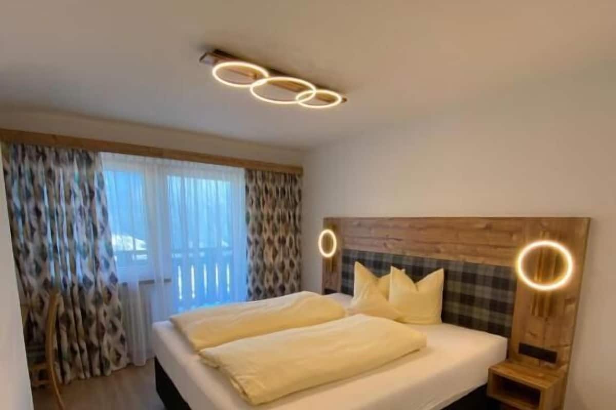 Un dormitorio con cama, cabecera de madera, mesitas de noche y una ventana con cortinas.