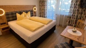 A hotel room with a bed, bedside tables, a small table with a chair, and a window with curtains. - Gasthof Pension Berghof (Hippach-Schwendberg)