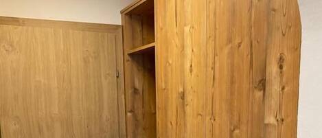 A wooden wardrobe with a door and a shelf, a wooden bench, and a small wooden stool.