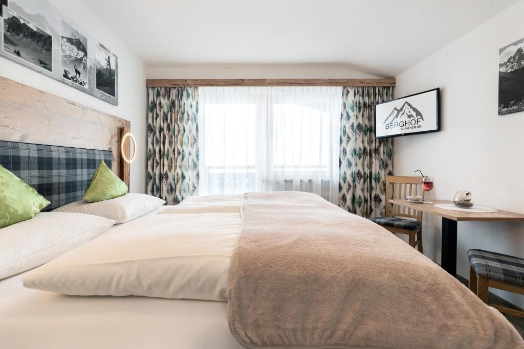A hotel room with a bed, a desk, a chair, and a window with curtains.