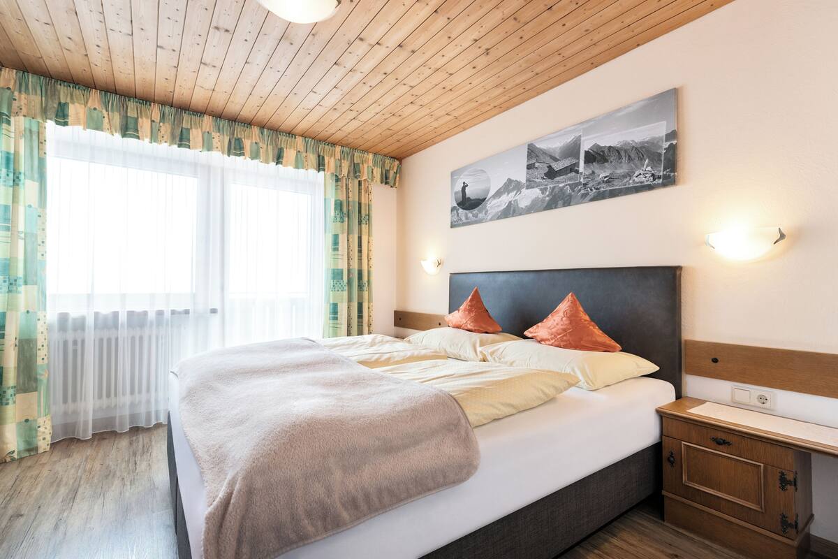 Una cama bien hecha con almohadas, una mesita de noche y una lámpara de pared.