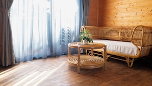 Una habitación con techo de madera, un sofá de mimbre, una mesa redonda con una planta y cortinas de encaje.
