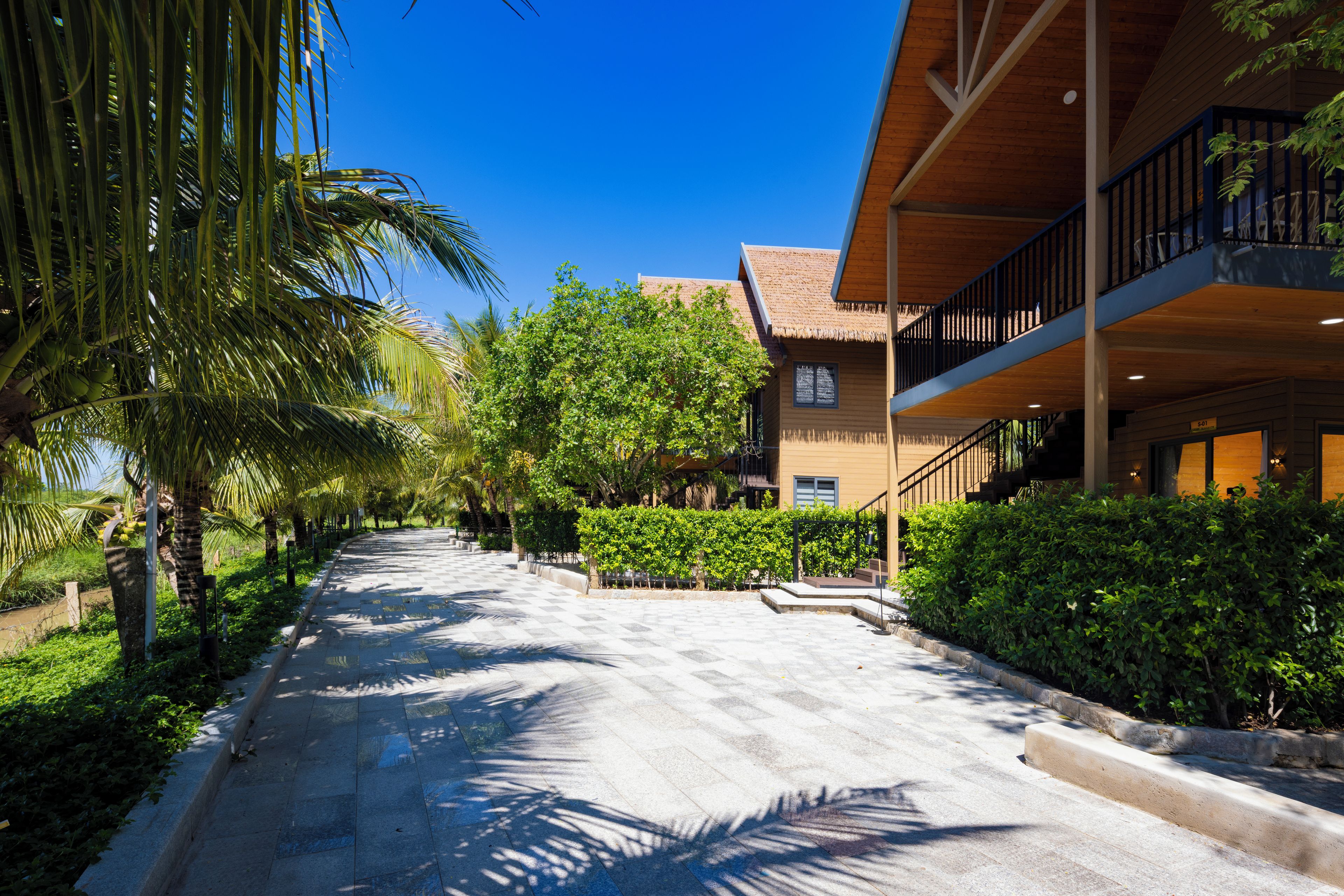 A paved pathway leading to a building with a balcony and a thatched roof.
