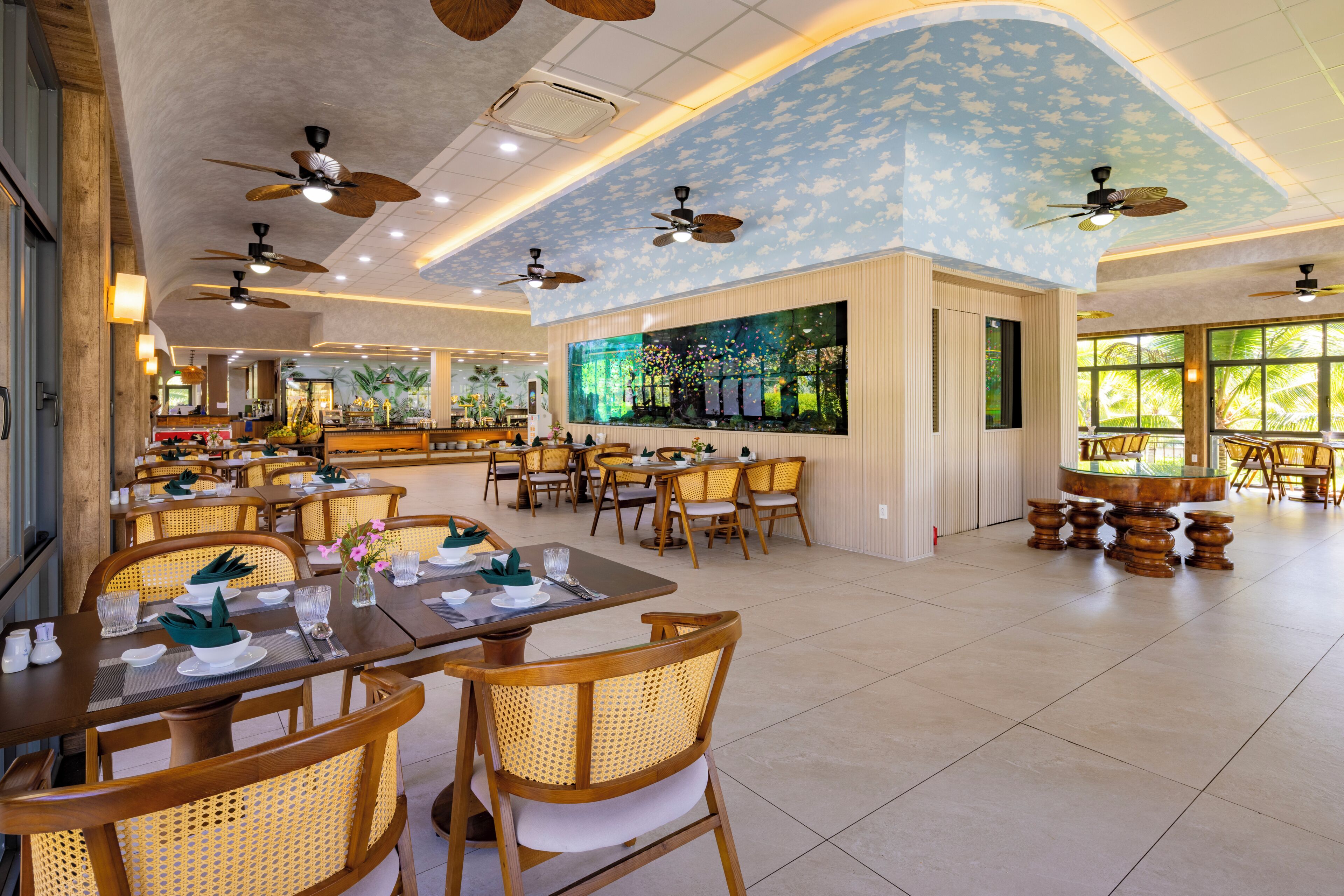 A spacious dining area with multiple tables and chairs, ceiling fans, and a large window providing natural light.