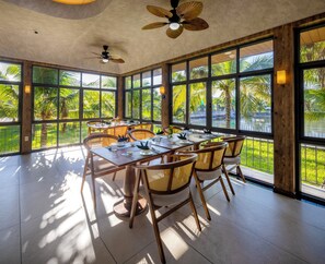 Un comedor amplio con una mesa grande y sillas, ventanas grandes con vistas a zonas verdes y ventiladores de techo.