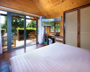 Habitación con una cama, un escritorio con computadora y vista a un jardín por una puerta corrediza.
