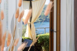 Ein Zimmer mit Blick auf einen See und grüne Landschaft, eine Tür und ein Fenster mit Vorhängen.