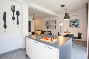 Eine moderne Küche mit Kochinsel, Essbereich mit Tisch und Stühlen sowie Wohnbereich mit Sofa und Wandbildern.