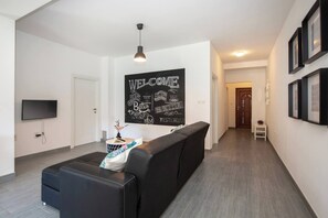 A modern living room with a black sofa, a flat-screen TV, a blackboard with motivational quotes, and a hallway leading to a door. - 210 Sea Side 2bedrooms Holiday Apartment SeaView (Duga Luka)