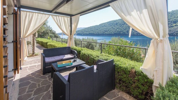 A covered outdoor seating area with wicker furniture, a stone floor, and a view of a lake and hills. - 210 Sea Side 2bedrooms Holiday Apartment SeaView (Duga Luka)