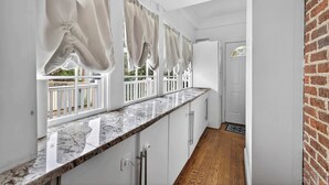 Eine Küche mit weißen Schränken, einer Marmorarbeitsplatte und Blick auf einen Balkon mit weißen Geländern.