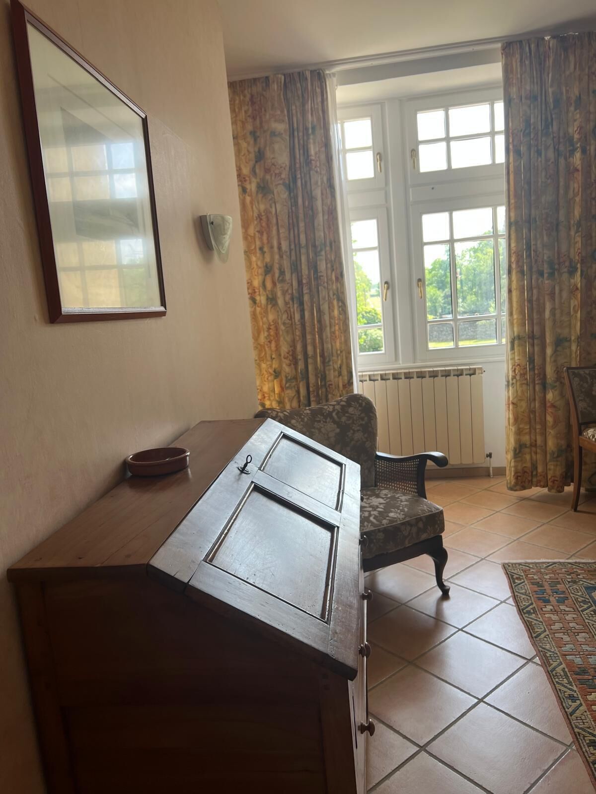 Una habitación con un escritorio de madera, una silla, un radiador y una ventana con cortinas.