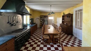 Una cocina con suelo a cuadros, una mesa de madera y sillas, una estufa y utensilios colgando.